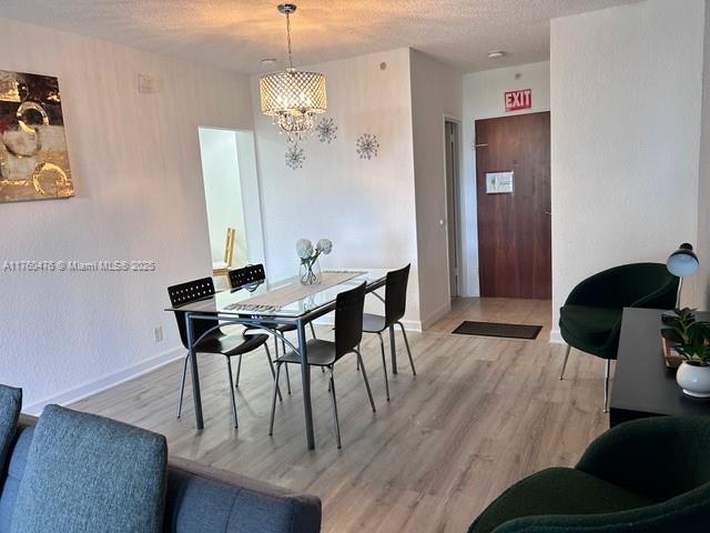 dining space with a textured ceiling, light wood-style flooring, baseboards, and a chandelier