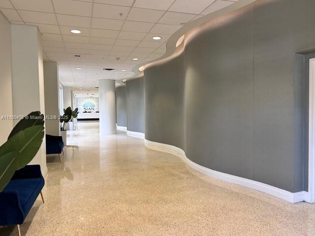 corridor with recessed lighting, speckled floor, a paneled ceiling, and baseboards