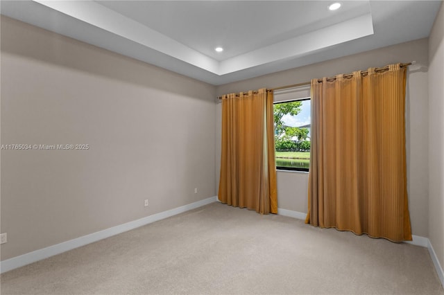 empty room featuring a raised ceiling, baseboards, light carpet, and recessed lighting