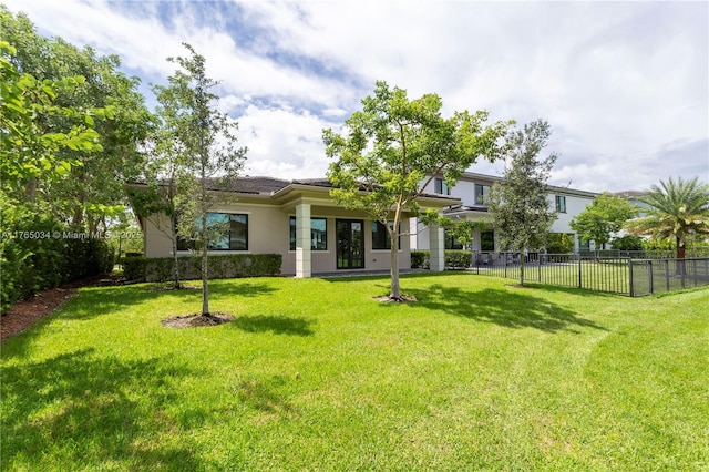 rear view of house with fence, stucco siding, and a yard