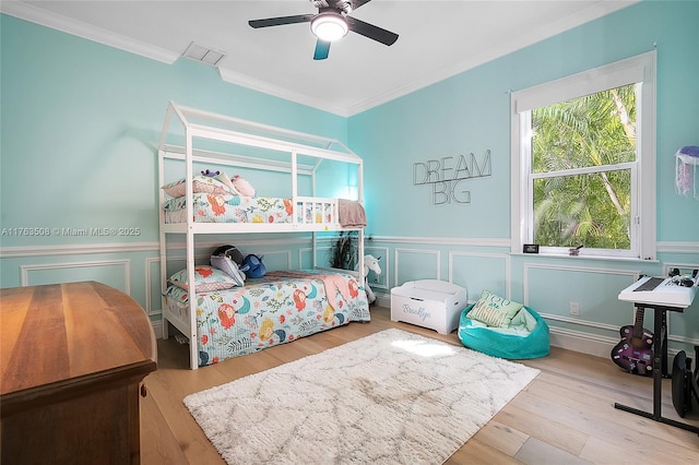 bedroom with ornamental molding, wainscoting, wood finished floors, and visible vents
