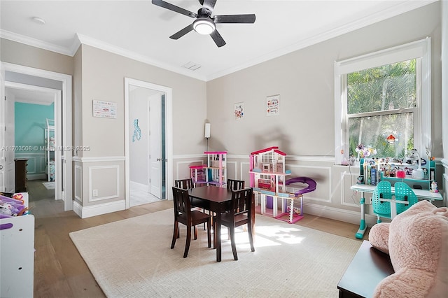 recreation room featuring ceiling fan, visible vents, crown molding, wood finished floors, and a decorative wall