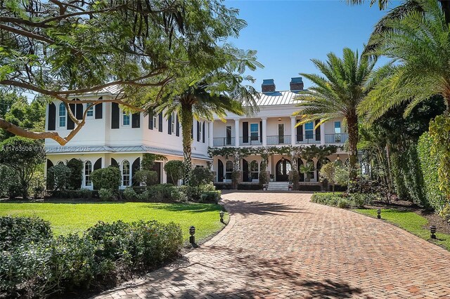 view of front of home featuring covered porch, a chimney, curved driveway, a balcony, and a front lawn