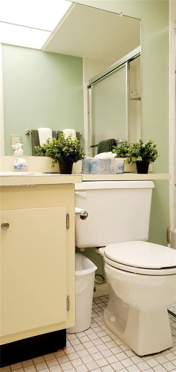 bathroom featuring a shower with door, tile patterned flooring, toilet, and vanity