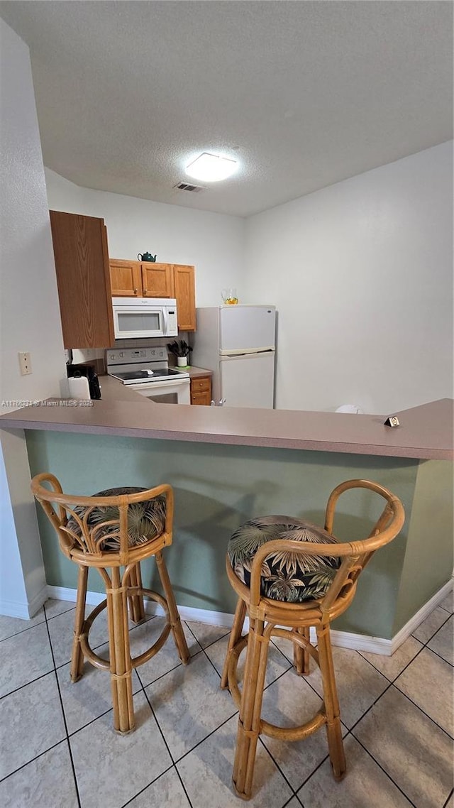 1013 Park Ridge Cir, Kissimmee, FL 34746 - kitchen featuring white appliances, visible vents, light tile patterned flooring, a textured ceiling, and a kitchen breakfast bar