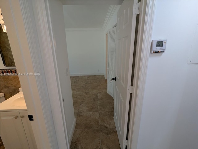hallway with a sink, crown molding, baseboards, and dark tile patterned flooring