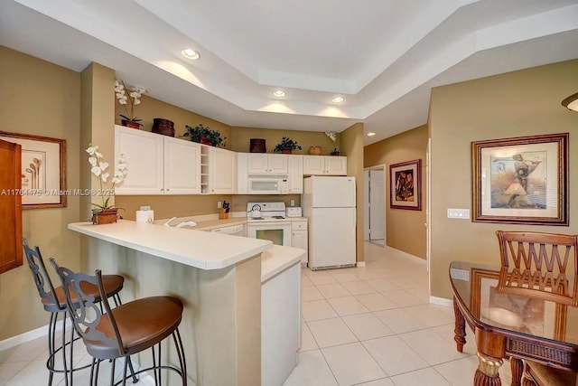 kitchen featuring light countertops, a kitchen bar, recessed lighting, a peninsula, and white appliances