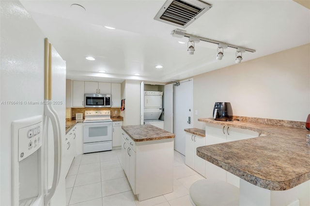kitchen with white appliances, visible vents, a kitchen island, stacked washer and dryer, and white cabinets