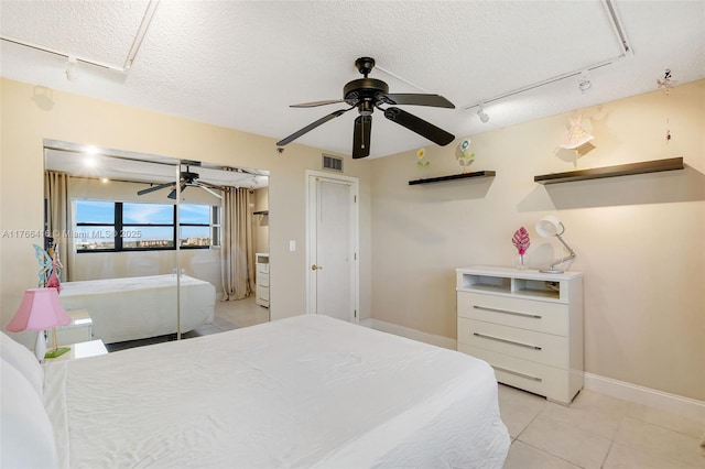 tiled bedroom with visible vents, track lighting, a textured ceiling, baseboards, and ceiling fan