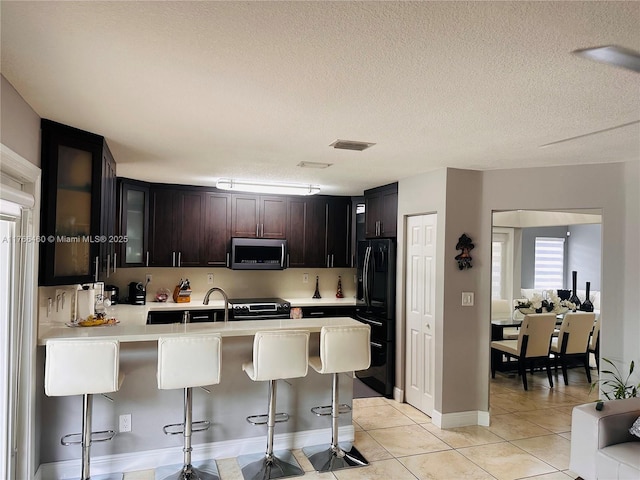 kitchen with black fridge, stainless steel microwave, range with electric stovetop, a peninsula, and light countertops