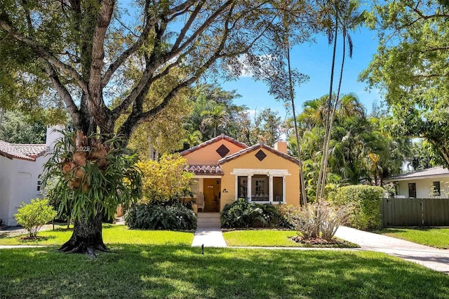 mediterranean / spanish home with a front lawn, fence, a tiled roof, stucco siding, and a chimney