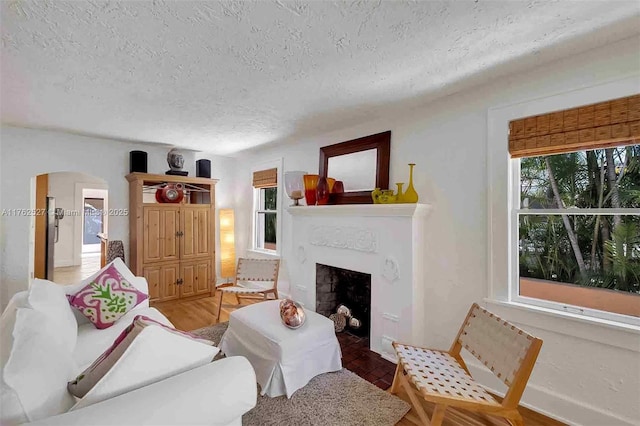 living area with visible vents, light wood-style flooring, a textured ceiling, arched walkways, and baseboards