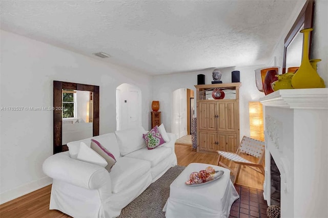 living area featuring arched walkways, a textured ceiling, light wood-style flooring, and a fireplace