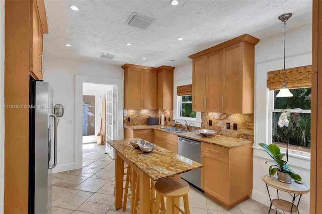 kitchen with tasteful backsplash, light stone countertops, stainless steel appliances, and a sink