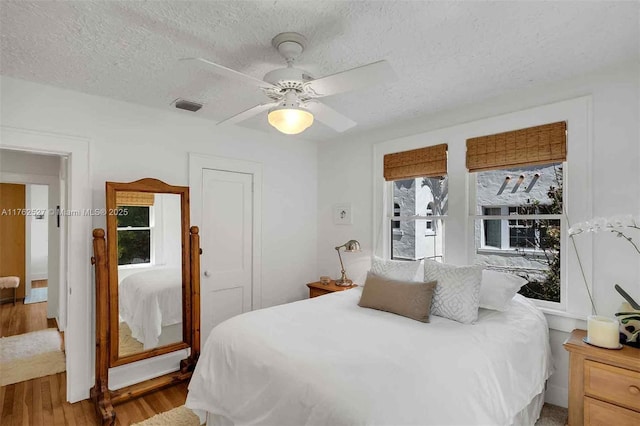bedroom with visible vents, a textured ceiling, ceiling fan, and wood finished floors