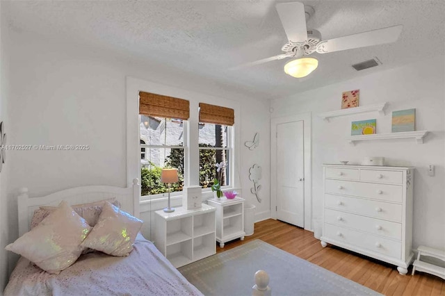 bedroom featuring light wood finished floors, visible vents, ceiling fan, arched walkways, and a textured ceiling