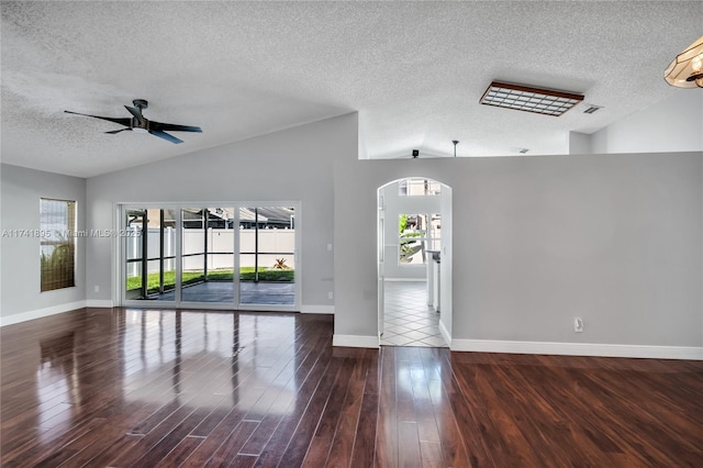 spare room with baseboards, a textured ceiling, lofted ceiling, arched walkways, and wood finished floors