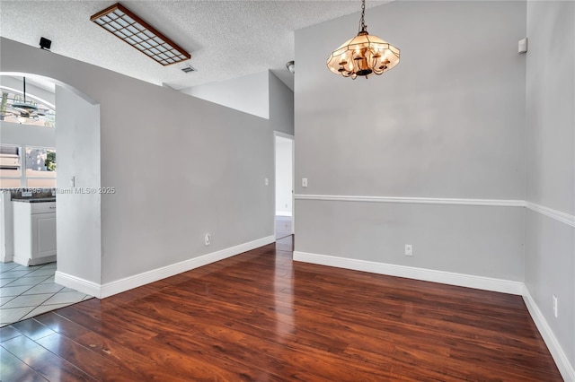 empty room with arched walkways, a textured ceiling, wood-type flooring, lofted ceiling, and baseboards