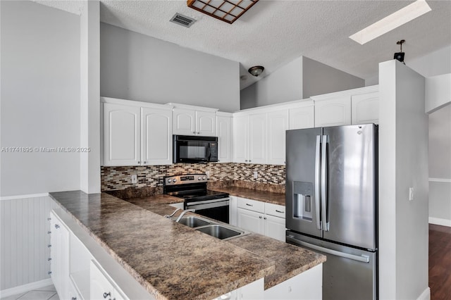 kitchen featuring visible vents, a sink, dark countertops, appliances with stainless steel finishes, and a peninsula