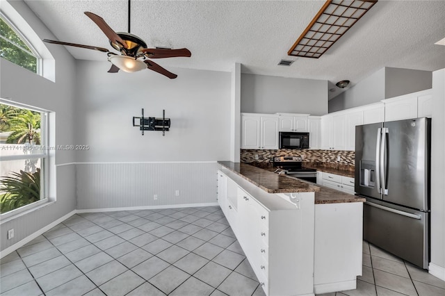 kitchen with a peninsula, light tile patterned floors, a ceiling fan, dark countertops, and stainless steel appliances