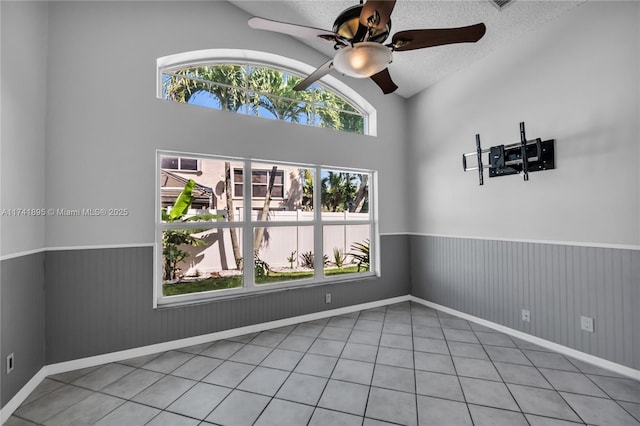 spare room with baseboards, a ceiling fan, vaulted ceiling, a wainscoted wall, and tile patterned flooring