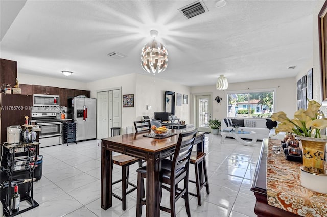 dining area featuring a chandelier, a textured ceiling, marble finish floor, and visible vents