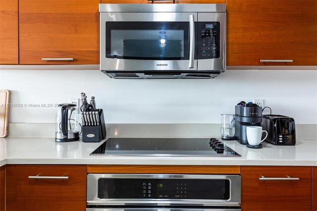 kitchen featuring oven, brown cabinets, modern cabinets, stainless steel microwave, and black electric cooktop