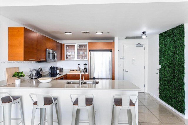 kitchen with visible vents, a sink, stainless steel appliances, a peninsula, and brown cabinetry