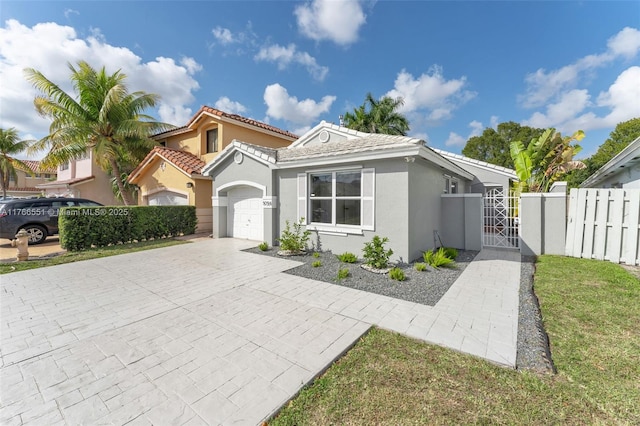 view of front of property with fence, stucco siding, decorative driveway, an attached garage, and a gate