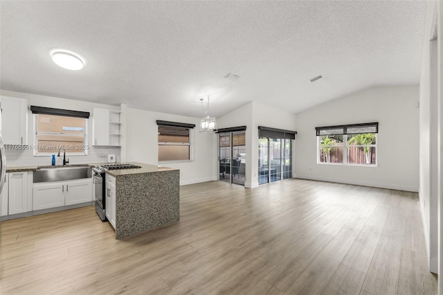 kitchen featuring a sink, white cabinets, light wood-style floors, gas range oven, and open floor plan