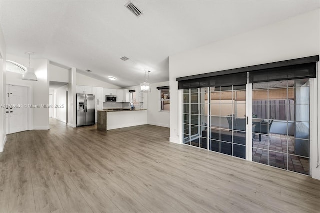 unfurnished living room with vaulted ceiling, baseboards, visible vents, and wood finished floors