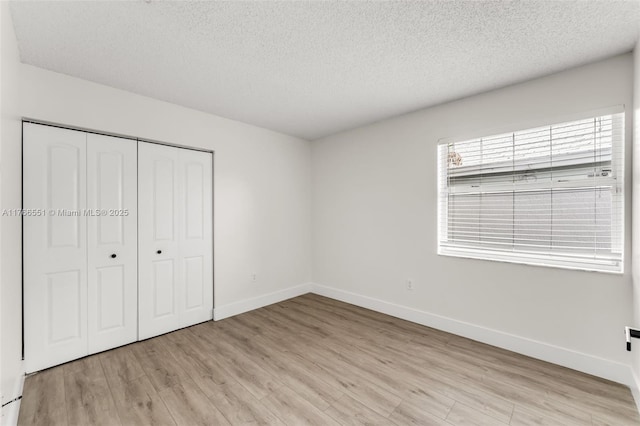 unfurnished bedroom featuring a closet, a textured ceiling, light wood-type flooring, and baseboards