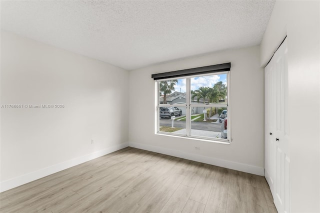 unfurnished bedroom with a closet, baseboards, a textured ceiling, and light wood finished floors