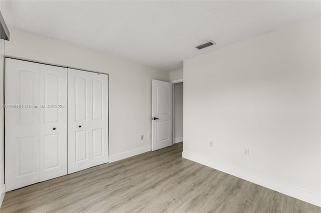 unfurnished bedroom featuring visible vents, baseboards, a closet, and light wood finished floors