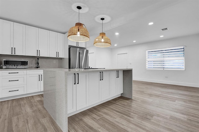 kitchen with visible vents, light wood-style flooring, a kitchen island, white cabinetry, and stainless steel appliances