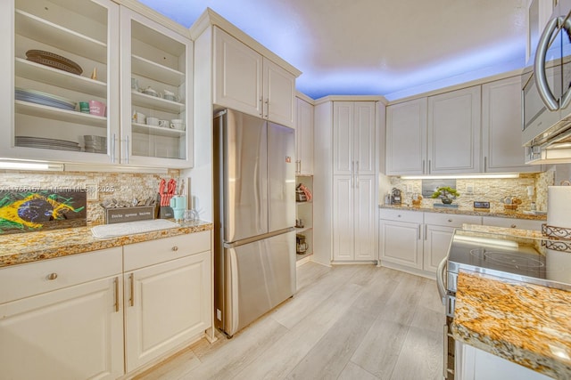 kitchen featuring tasteful backsplash, light wood-type flooring, stainless steel appliances, and glass insert cabinets