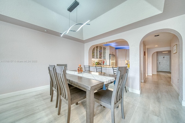 dining space with light wood finished floors, arched walkways, a textured wall, and baseboards