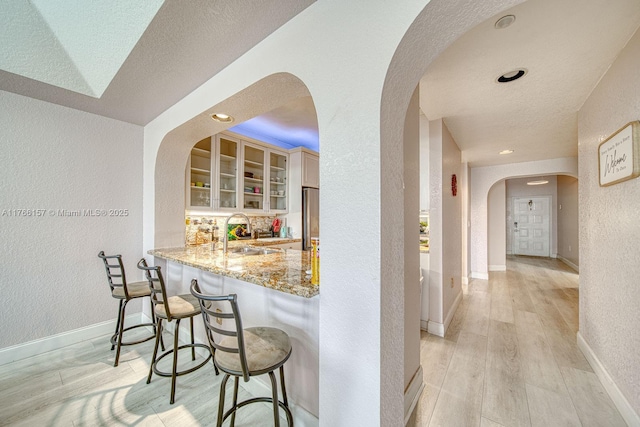 interior space featuring arched walkways, freestanding refrigerator, light wood-style floors, a textured wall, and a sink