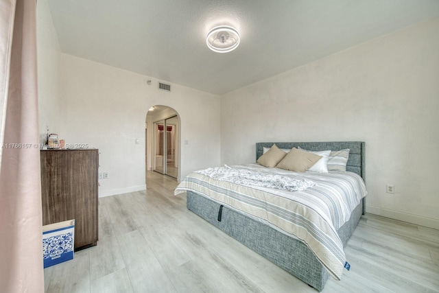bedroom featuring baseboards, visible vents, arched walkways, and wood finished floors