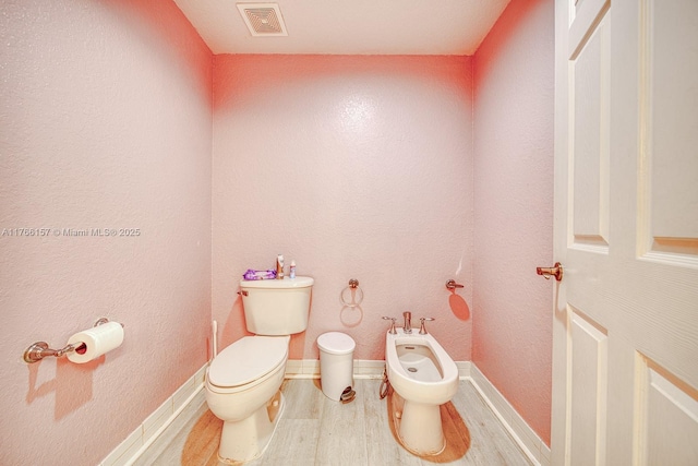 bathroom featuring wood finished floors, visible vents, toilet, and a bidet