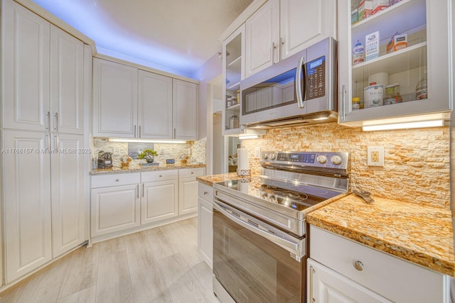 kitchen with light stone countertops, glass insert cabinets, decorative backsplash, appliances with stainless steel finishes, and white cabinets