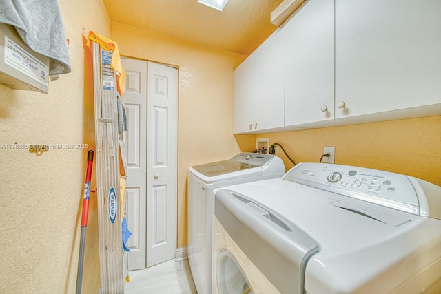 washroom featuring cabinet space, a textured wall, and washing machine and dryer