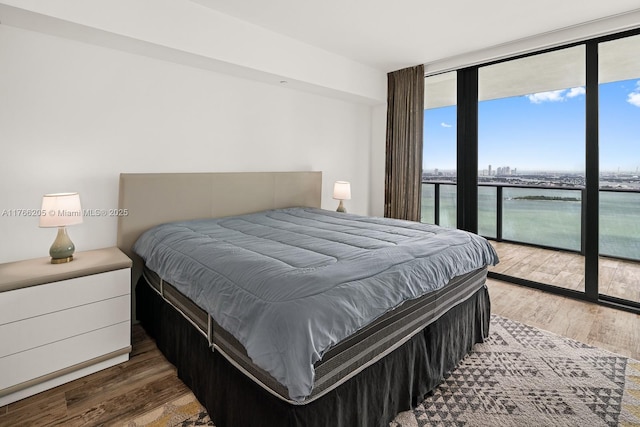 bedroom with access to exterior, a wall of windows, wood finished floors, and a water view