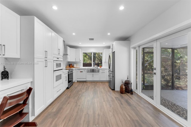 kitchen with white cabinets, light wood-type flooring, white appliances, and recessed lighting