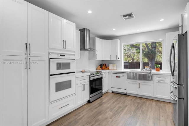 kitchen with wall chimney exhaust hood, light wood-type flooring, visible vents, appliances with stainless steel finishes, and a sink