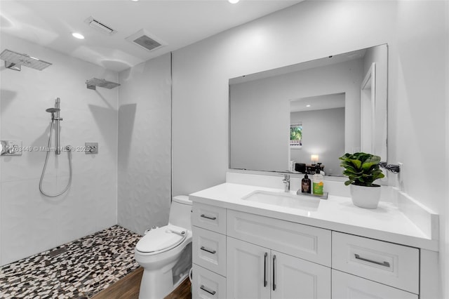 full bath with toilet, tiled shower, vanity, and visible vents