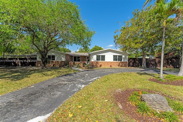ranch-style home with aphalt driveway, stucco siding, fence, a front lawn, and brick siding