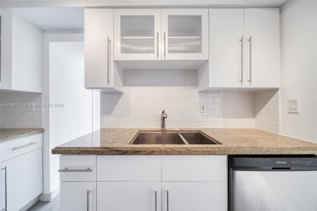 kitchen with light stone counters, white cabinets, dishwasher, and a sink