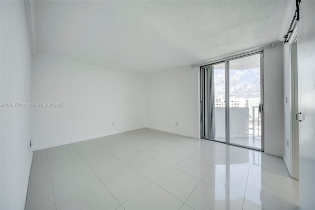 empty room with a textured ceiling, light tile patterned floors, baseboards, and expansive windows