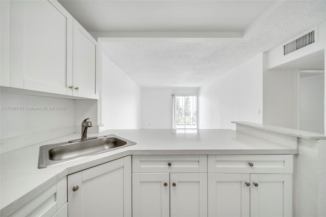 kitchen featuring visible vents, a sink, white cabinetry, a peninsula, and light countertops
